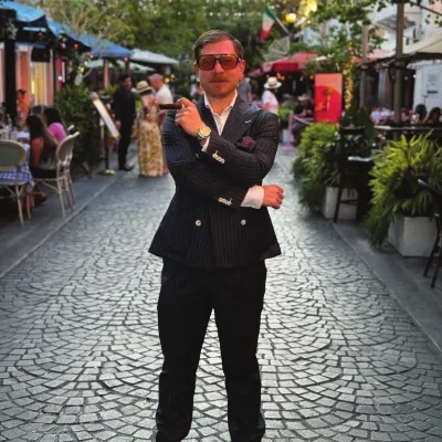 Joshua Habursky in a navy suit holding a cigar on a cobblestone street