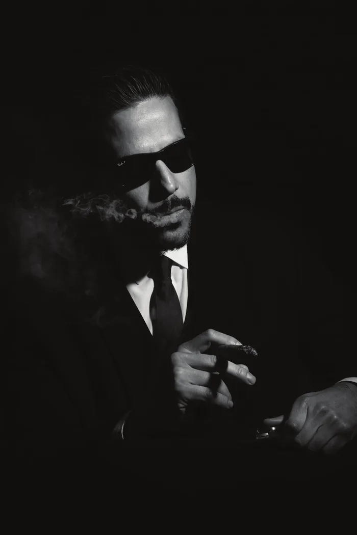 Ricardo Carioni smoking a cigar, black and white portrait on a dark background
